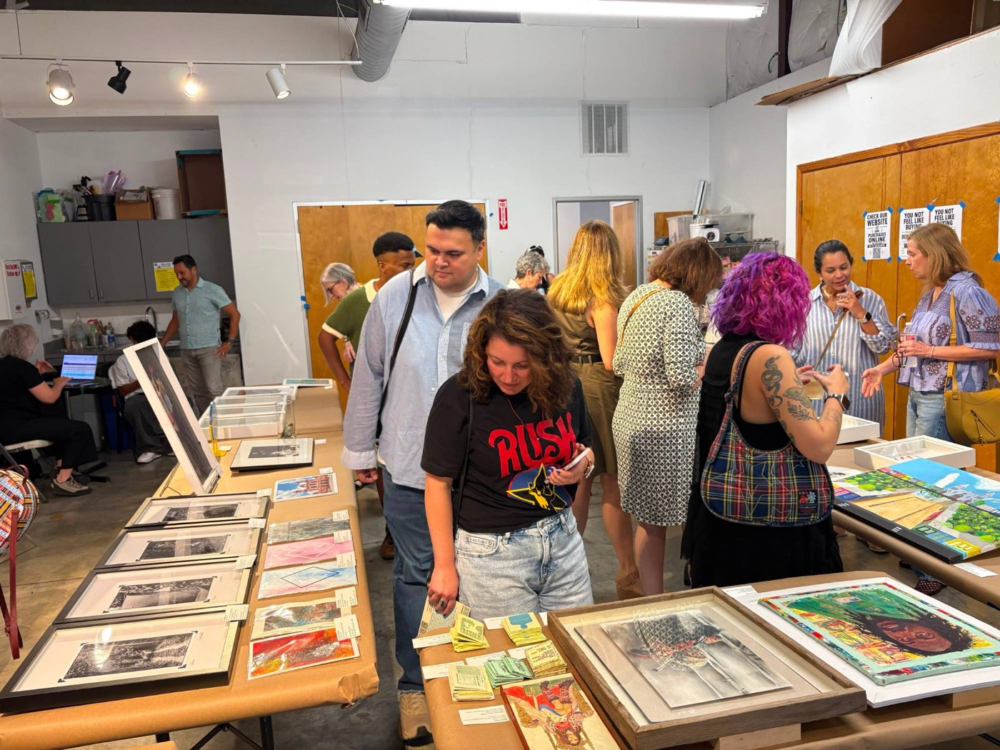 Visitors browsing artworks laid out on tables at the Houston Art Fair for Venezuela